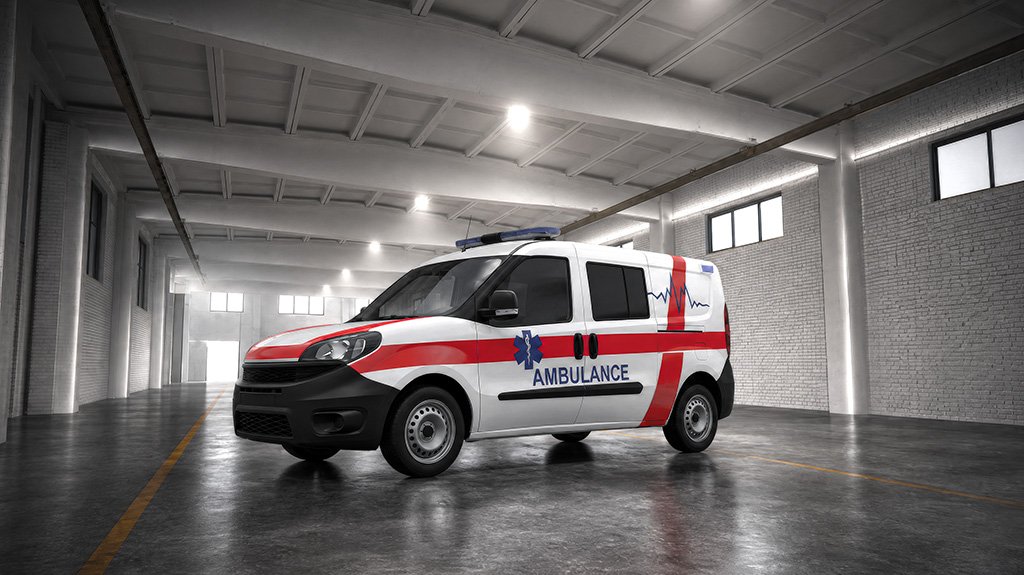 A white and red ambulance parked in a large, well-lit warehouse or garage, with the word "AMBULANCE" written on the side.