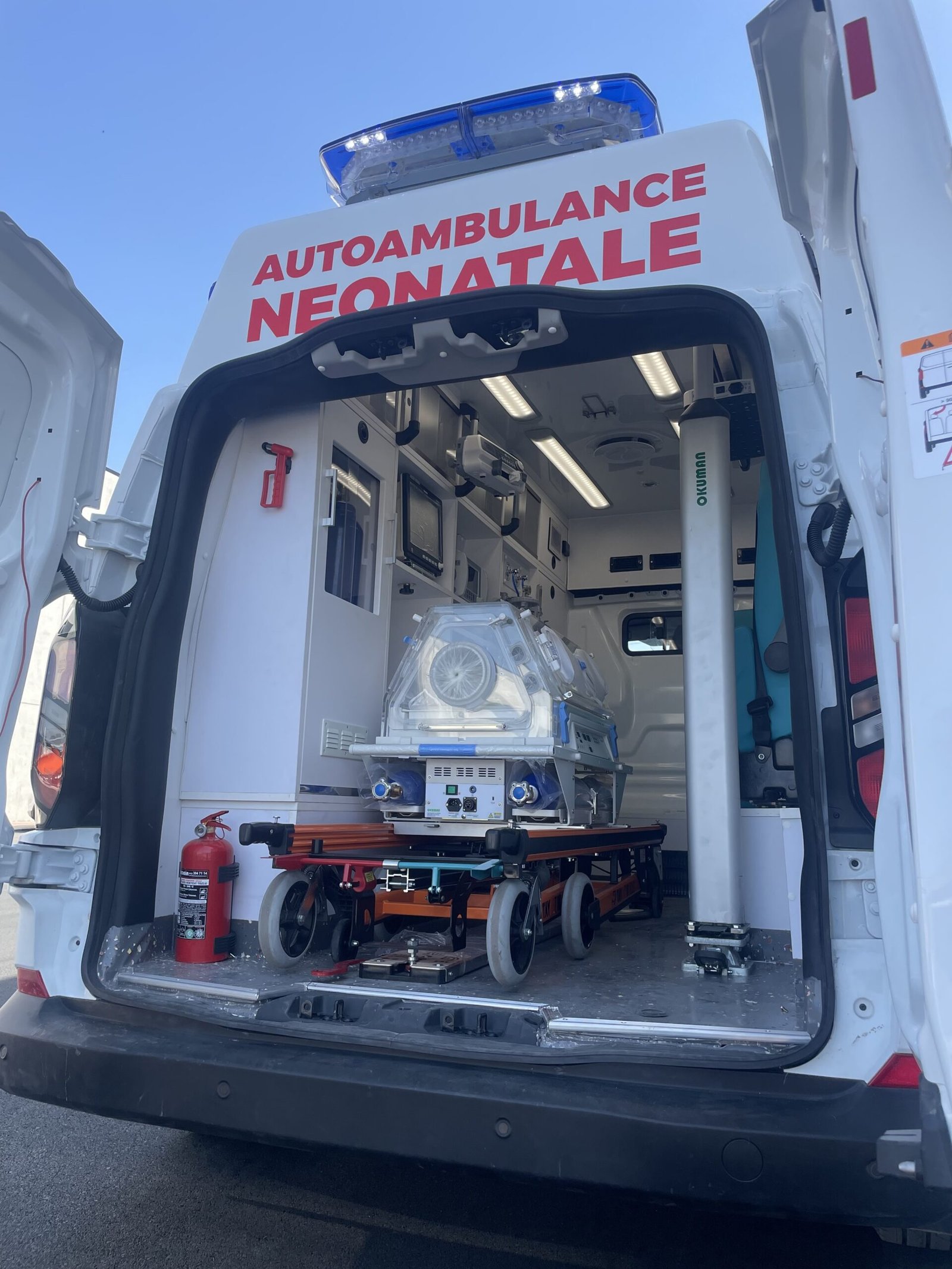 A white ambulance parked in a lot, with its rear doors open to reveal a medical bed inside.