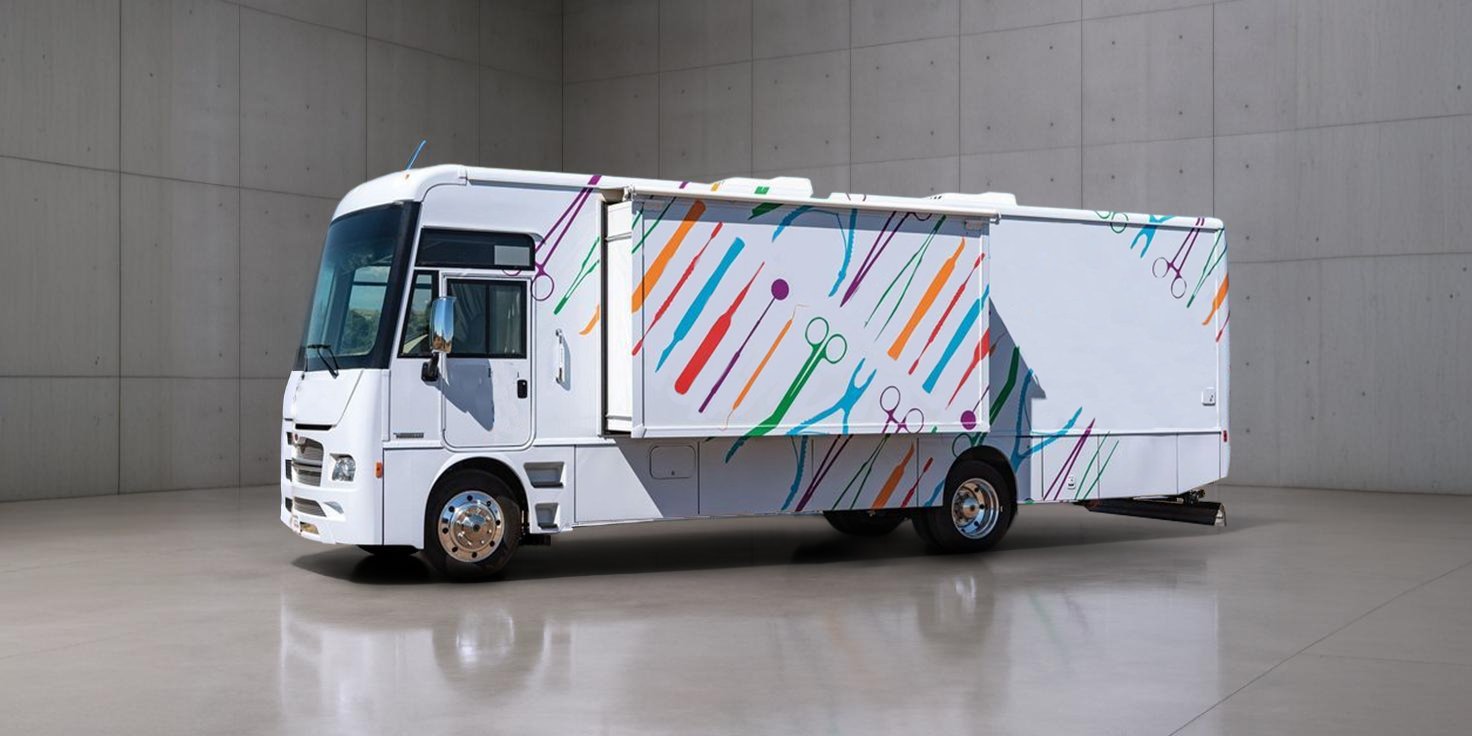 A white, rectangular RV with a colorful design parked in a gray room with a shiny floor.