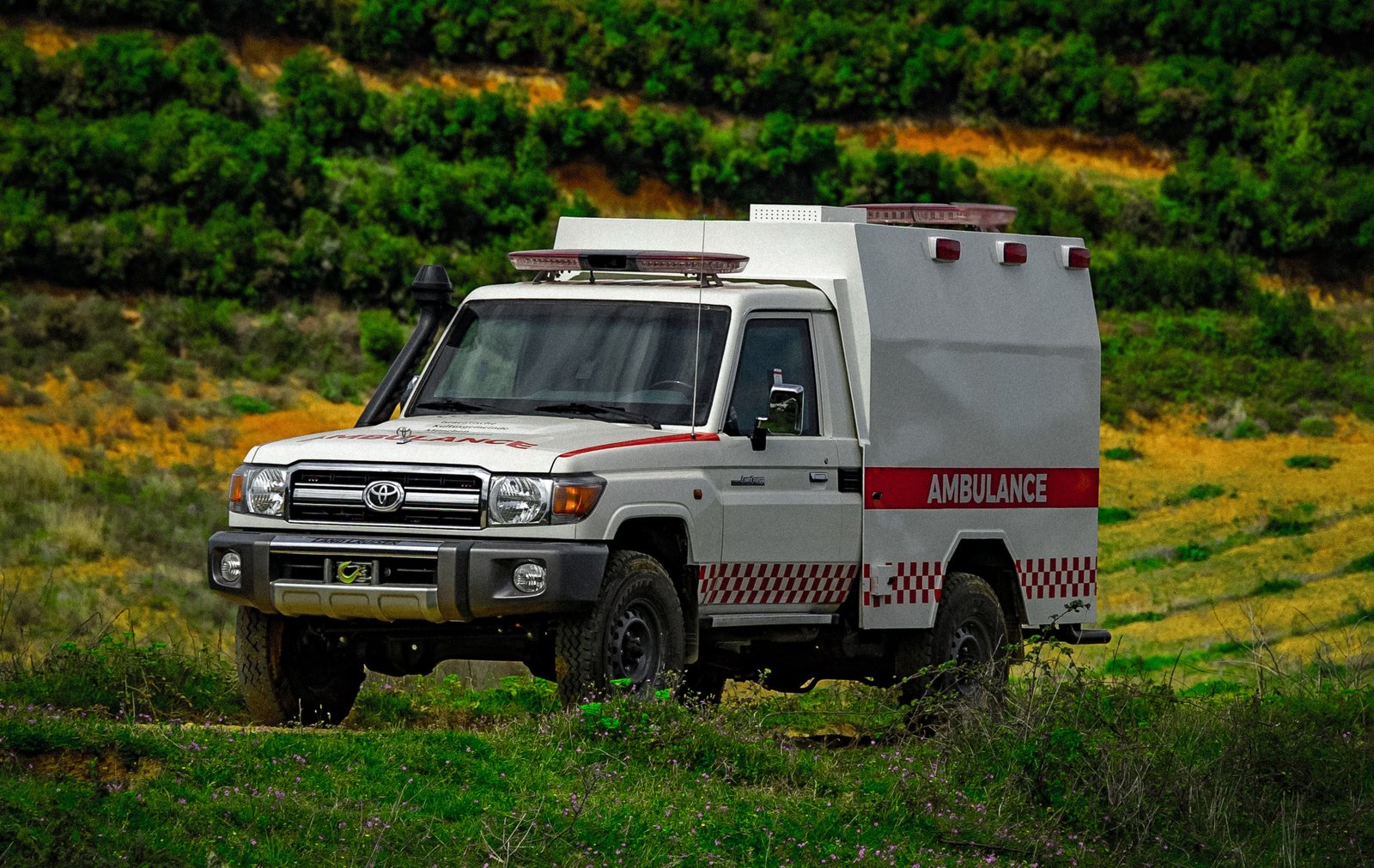 A white ambulance with red detailing is parked in a grassy field.
